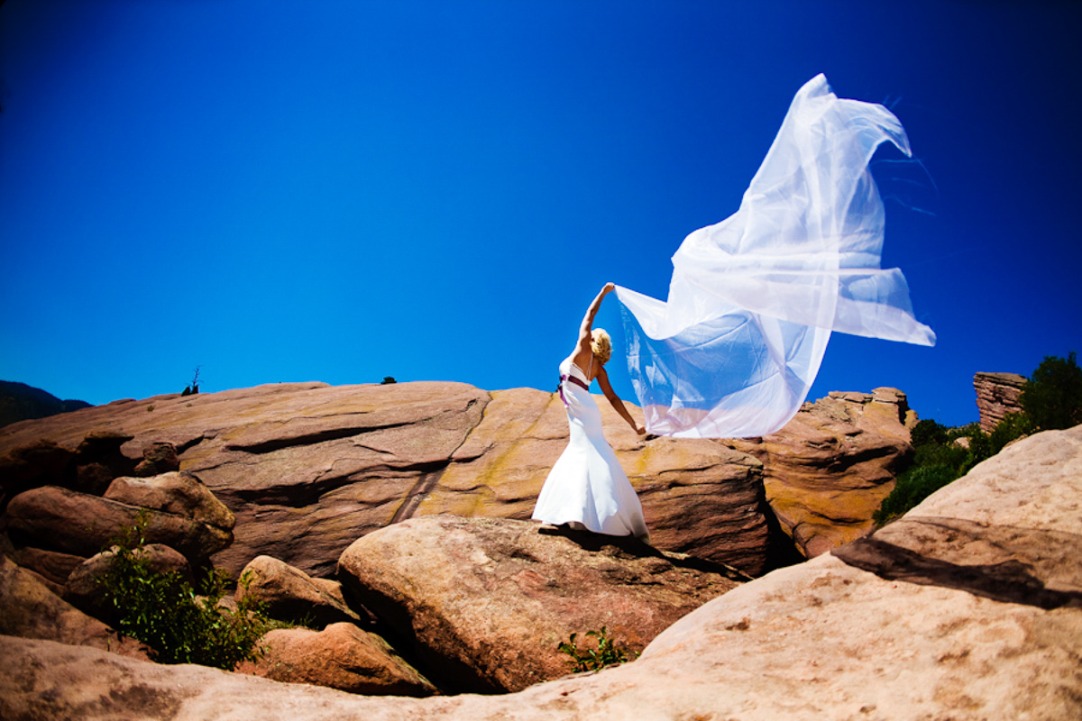 Model Renae Vespremi on a red rock ridge in a white gown, veil extended in the wind against a deep blue sky