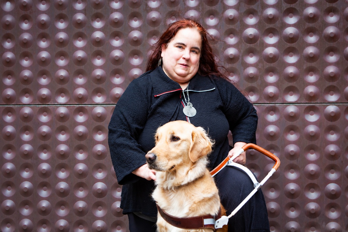 Maia, co-chair of the Access Advisors, with her golden retriever guide dog in front of the copper wall at the de Young