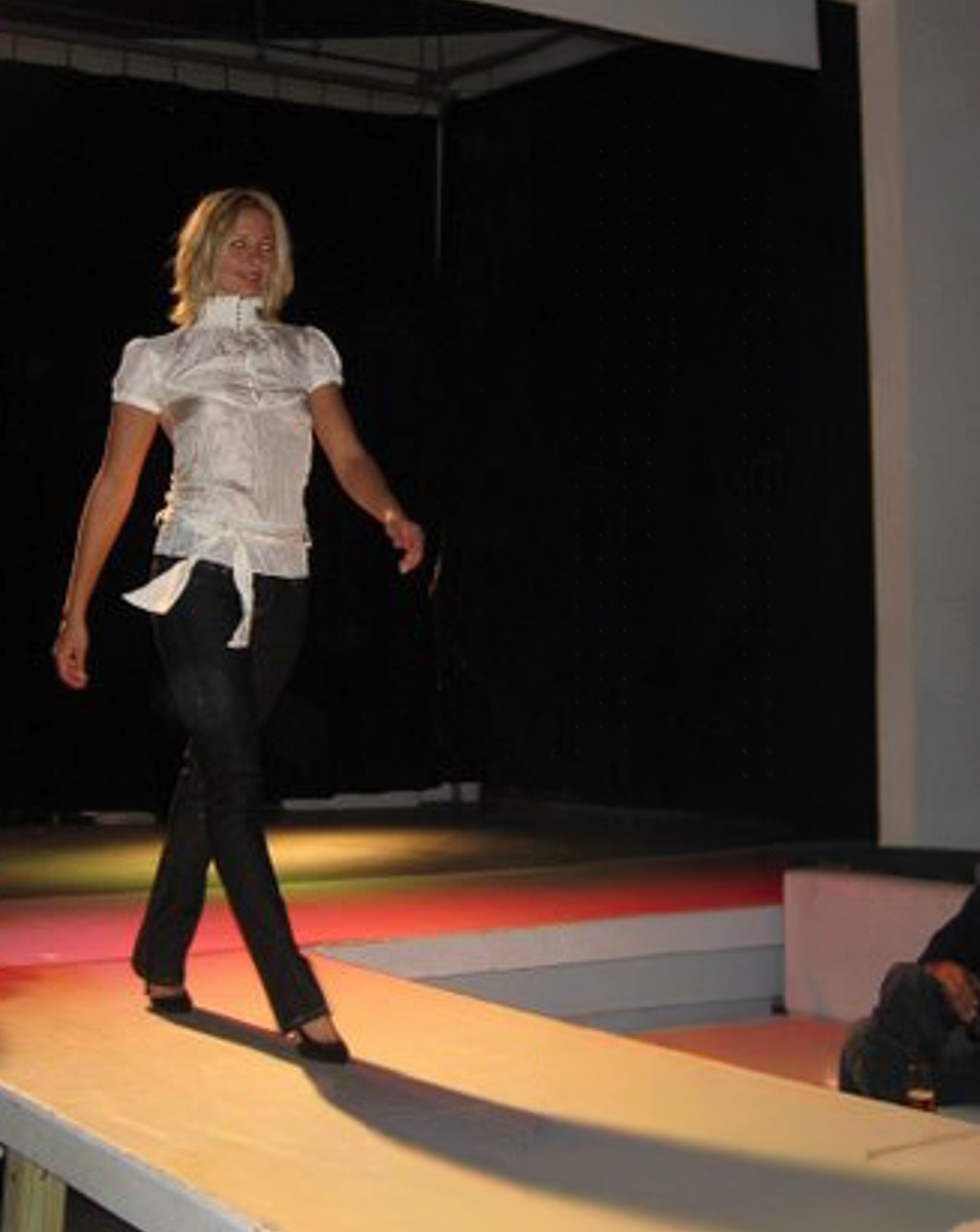Model Renae Vespremi walking a lit runway in a white blouse and dark denim
